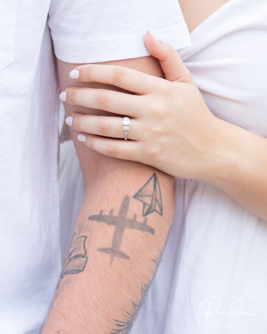 A womans hand with a ring rests on a mans tattooed arm, showing a paper airplane and airplane tattoo.
