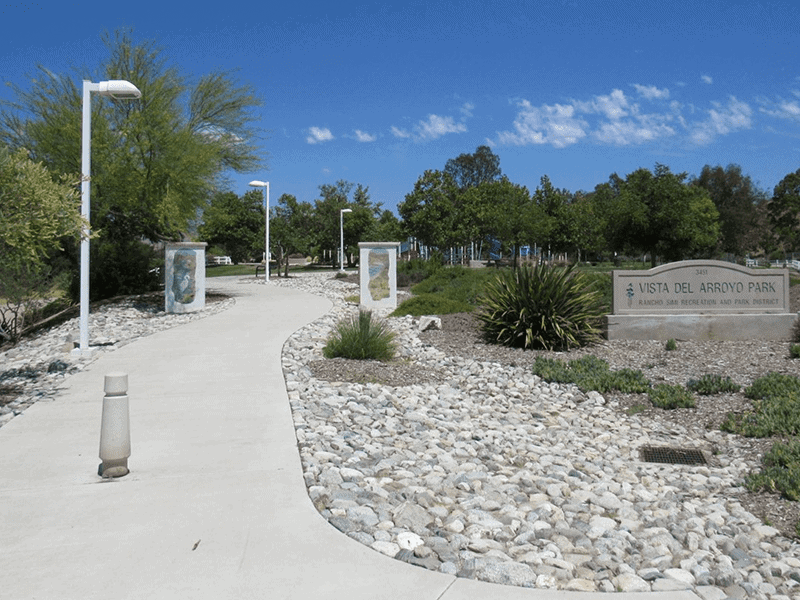 Vista Del Arroyo Park sign with a paved path, rocks, and plants next to it